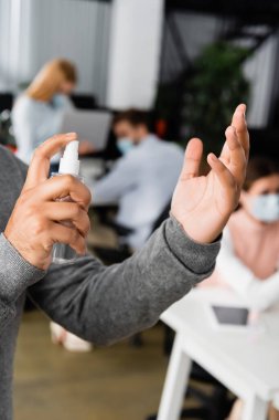 Ofiste bulanık arka planda iş arkadaşlarının yanında el dezenfektanı kullanan Hintli işadamı görüşü. 
