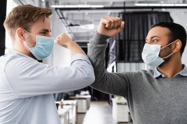 Multiethnic businessmen in medical masks giving high five with elbows  clipart