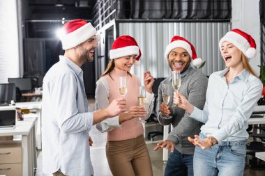 Noel Baba şapkalı neşeli çoklu etnik iş adamları ofiste şampanya kadehleriyle eğleniyorlar. 