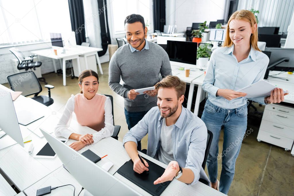 Smiling multicultural businesspeople using graphics tablet and computer in office 