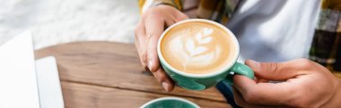 cropped view of man holding cup of coffee with latte art, banner clipart