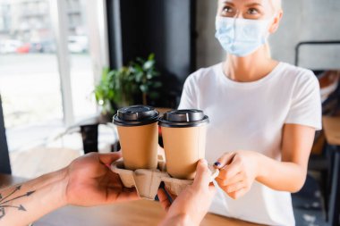 Barista 'nın tıbbi maskeli bir kadına kahve verirken çekilmiş görüntüsü.