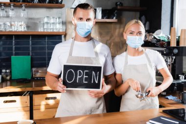 Tıbbi maske takan genç barista. Yanında açık harflerle iskele filtresi olan bir meslektaşı var.