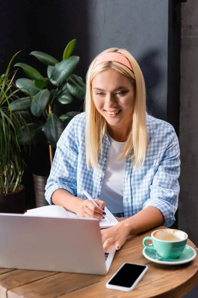 Mengetik Freelancer Tersenyum Laptop Dekat Cangkir Kopi Dan Smartphone Dengan — Stok Foto