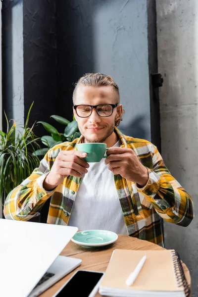 Pleased Freelancer Enjoying Flavor Coffee While Holding Cup Laptop Smartphone — Stock Photo, Image