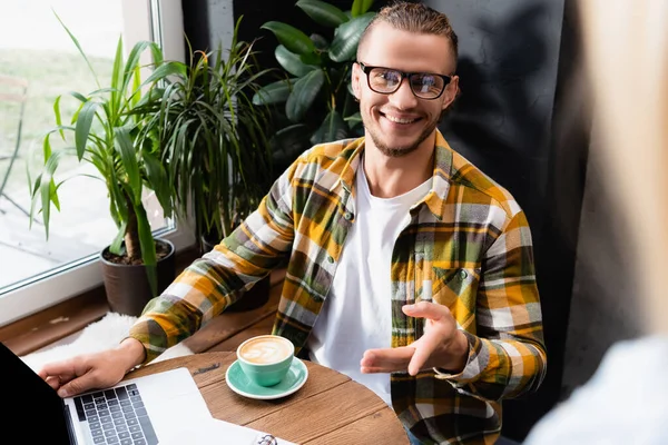 戴着眼镜 穿着格子花衬衫的快乐的自由职业者 手拿着咖啡杯和咖啡店里的笔记本电脑 — 图库照片