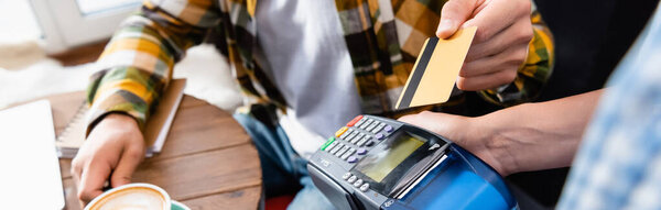 cropped view of man with credit card near waiter holding payment terminal, banner