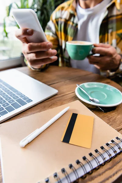 Częściowy Widok Freelancer Trzyma Filiżankę Kawy Smartfona Pobliżu Laptopa Notebooka — Zdjęcie stockowe