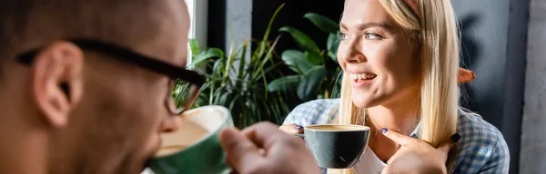 手前のぼやけたコーヒーを飲みながらお友達の近くでカップを持っている陽気な女性 — ストック写真