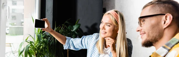 Cheerful Blonde Woman Taking Selfie Mobile Phone Friend Blurred Foreground — Stock Photo, Image