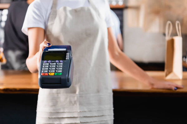 cropped view of barista holding payment terminal, blurred background