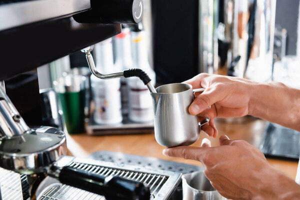 cropped view of barista holding metallic milk mug near steamer of coffee machine