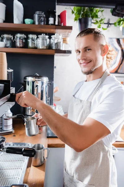 Kahve Makinesinin Yanında Metalik Süt Bardağı Tutarken Kameraya Bakan Gülümseyen — Stok fotoğraf