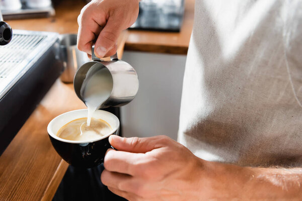 partial view of barista adding milk into cup of coffee 