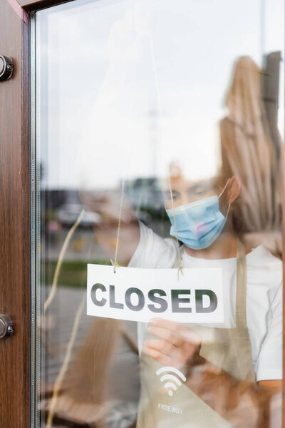 waiter in medical mask hanging card with closed lettering on cafe door