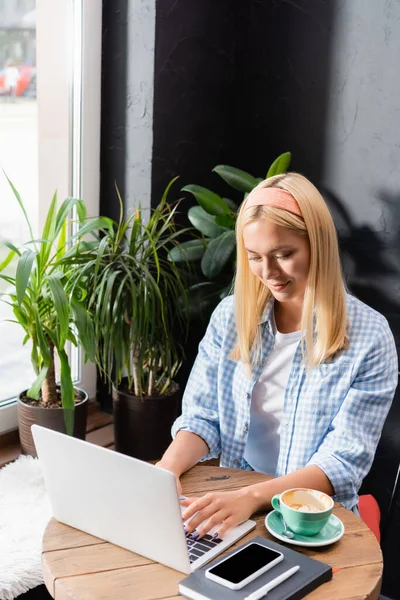 Sonriente Freelancer Rubia Camisa Cuadros Escribiendo Portátil Cerca Taza Café — Foto de Stock