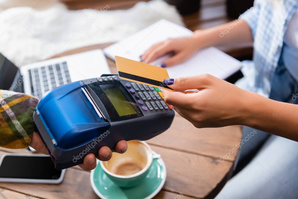 cropped view of woman holding credit card near waiter with payment terminal