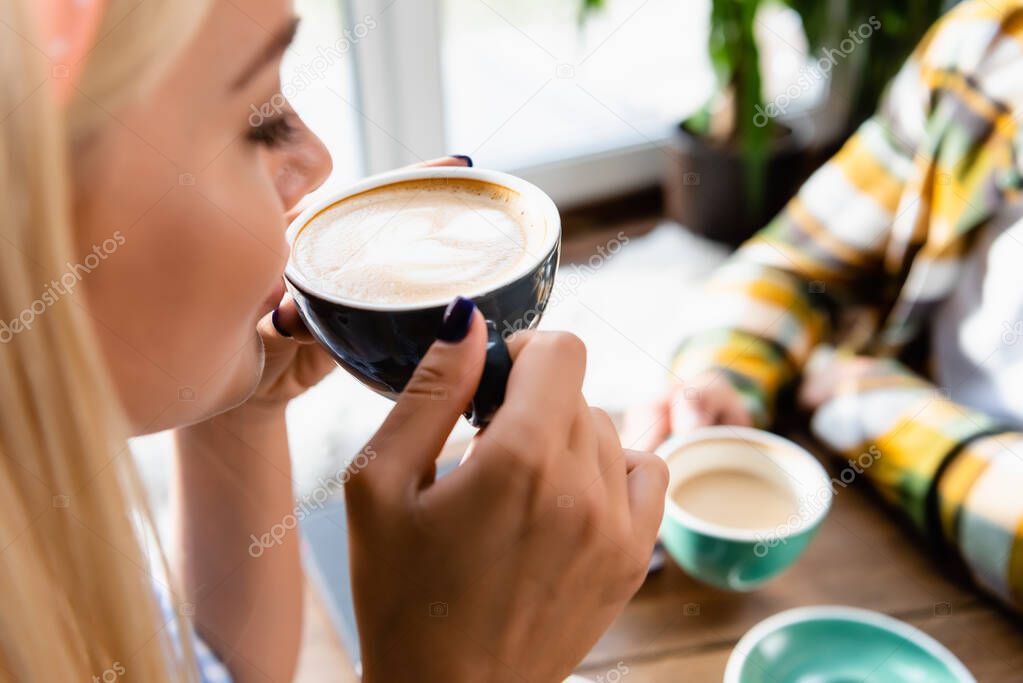 cropped view of woman drinking coffee near man on blurred background in cafe