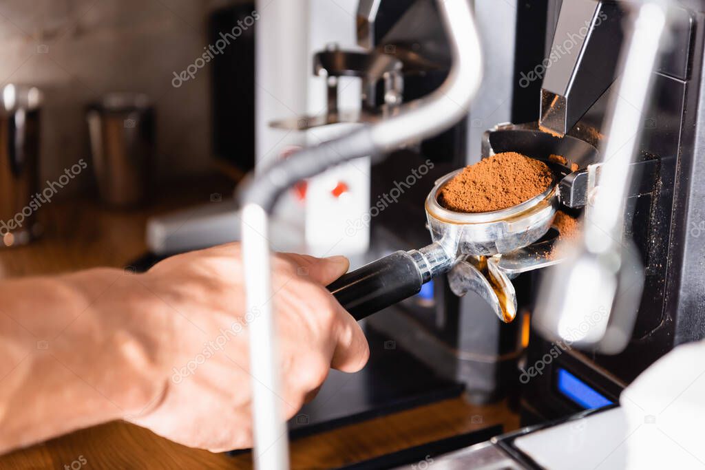 cropped view of barista holding portafilter near coffee machine, blurred foreground