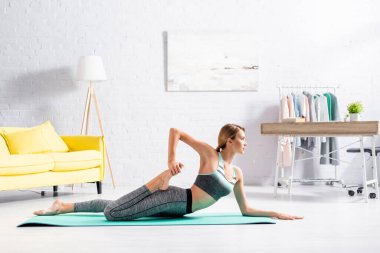 Çıplak ayaklı sporcu kadın spor minderinde yatarken yoga yapıyor. 