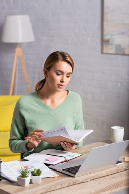 Blonde Freelancer 'ın elinde belgeler ve dizüstü bilgisayarla masadaki bulanık önplan. 