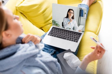 Bilgisayarında dijital tabletli doktor termometresi olan hasta bir kadının evinde görüntülü konuşma yapıyor. 