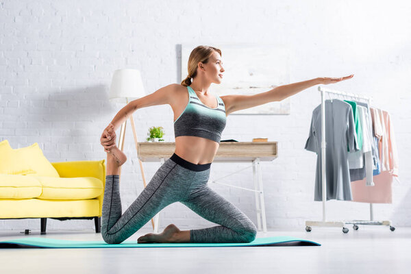 Fit sportswoman stretching while practicing yoga on mat at home 