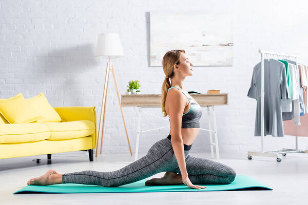 Side view of blonde sportswoman practicing yoga with closed eyes on fitness mat 