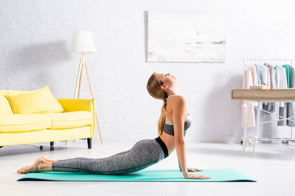 Woman in sportswear doing yoga asana with closed eyes on fitness mat 