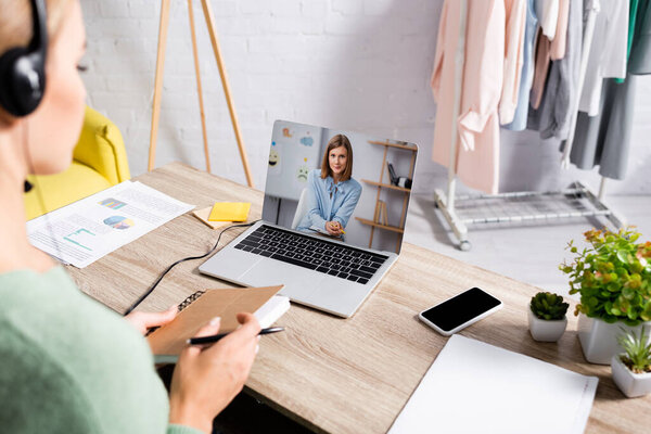 Молодая женщина с наушниками и с ноутбуком во время вебинара на ноутбуке дома 