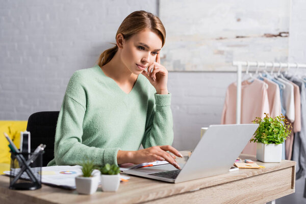 Молодой фрилансер, использующий ноутбук рядом с документами и растениями на размытом переднем плане дома 