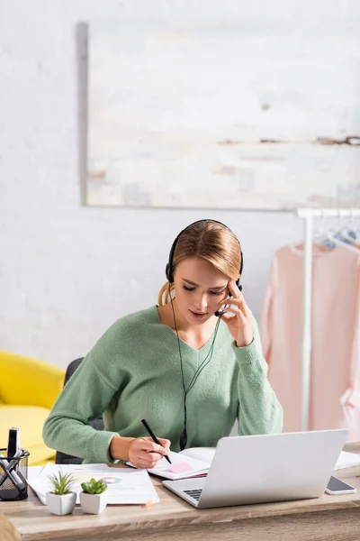 Freelancer Usando Fone Ouvido Enquanto Escreve Notebook Perto Laptop Primeiro — Fotografia de Stock