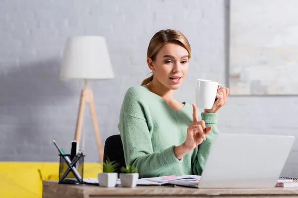 Freelancer Con Taza Apuntando Con Dedo Durante Videollamada Portátil Primer —  Fotos de Stock