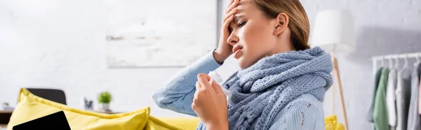 Ill woman in scarf holding napkin near laptop at home, banner