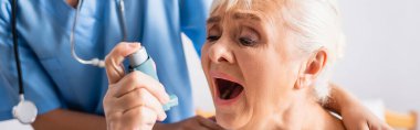 elderly woman with open mouth suffering from asthma attack and using inhaler near nurse on blurred background, banner clipart