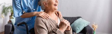cropped view of nurse touching shoulders of laughing disabled woman, banner clipart