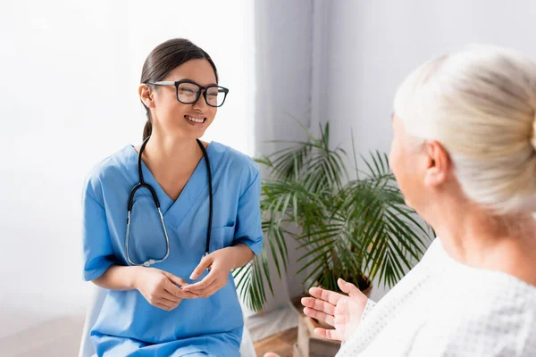 Cheerful Asian Nurse Eyeglasses Smiling Conversation Senior Woman Clinic Blurred — Stock Photo, Image