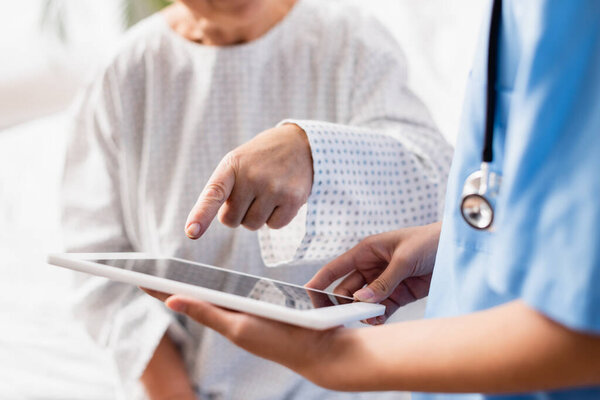 частичный взгляд пожилой женщины, указывающей пальцем на цифровой планшет в руках медсестры, избирательный фокус