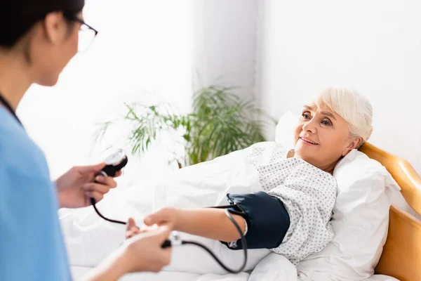 Junge Krankenschwester Misst Blutdruck Lächelnder Seniorin Mit Tonometer Verschwommener Vordergrund — Stockfoto