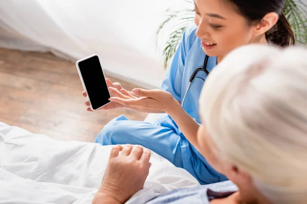 Над Головой Вид Улыбающейся Азиатской Медсестры Указывающей Мобильный Телефон Рядом — стоковое фото