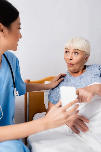 Amazed Elderly Woman Pointing Smartphone Young Asian Nurse Blurred Foreground — Stock Photo, Image