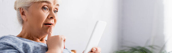 изумленная пожилая женщина касаясь губ при использовании смартфона в больнице, баннер
