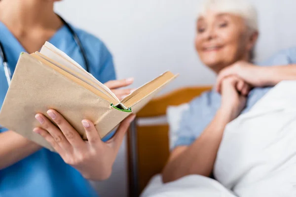 Nurse Reading Book Excited Elderly Woman Clinic Blurred Foreground — Stock Photo, Image