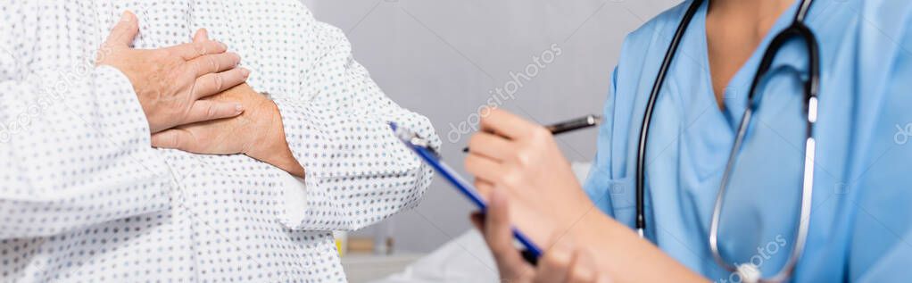 cropped view of senior woman touching chest while suffering from gasp attack near nurse writing on clipboard, blurred foreground, banner
