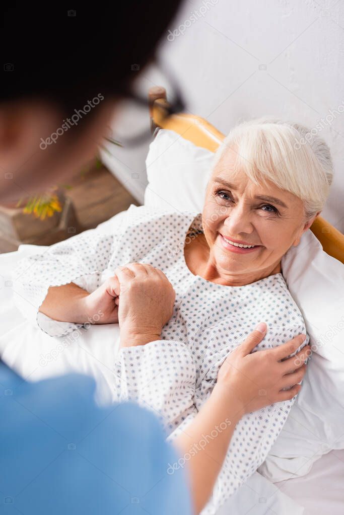 overhead view of nurse touching smiling elderly woman, blurred foreground