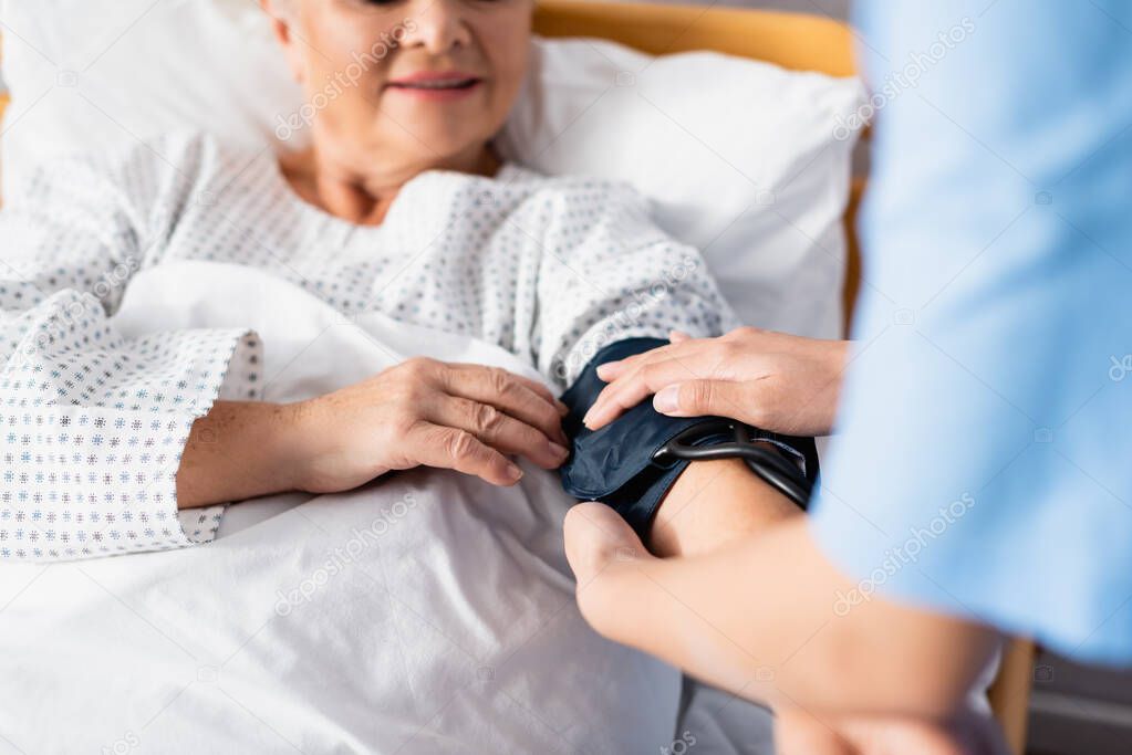 cropped view of nurse fixing cuff of tonometer on arm of elderly woman, selective focus