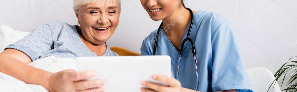 cheerful nurse and happy elderly woman using digital tablet together, banner