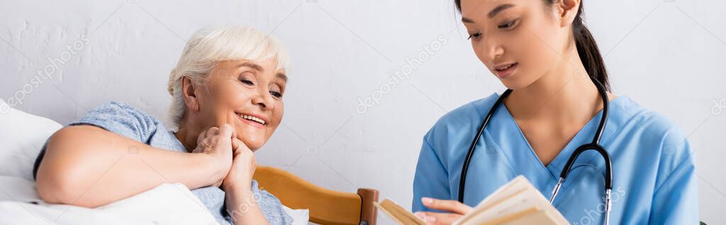 young asian nurse reading book to happy aged woman in hospital, banner