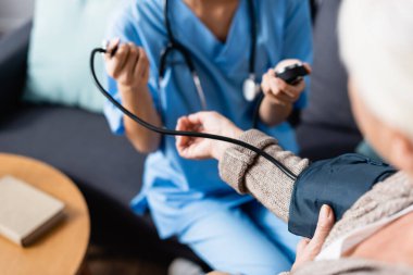 selective focus of elderly woman holding cuff of tonometer while nurse measuring her blood pressure clipart