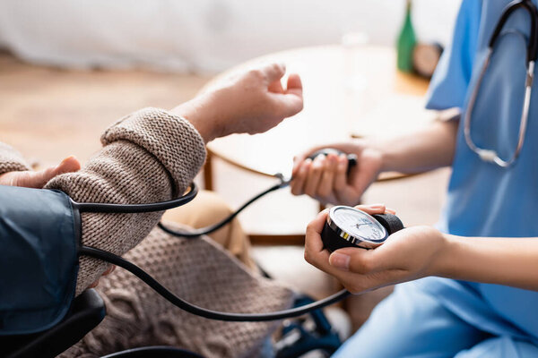 partial view of young nurse measuring blood pressure of senior woman, blurred background